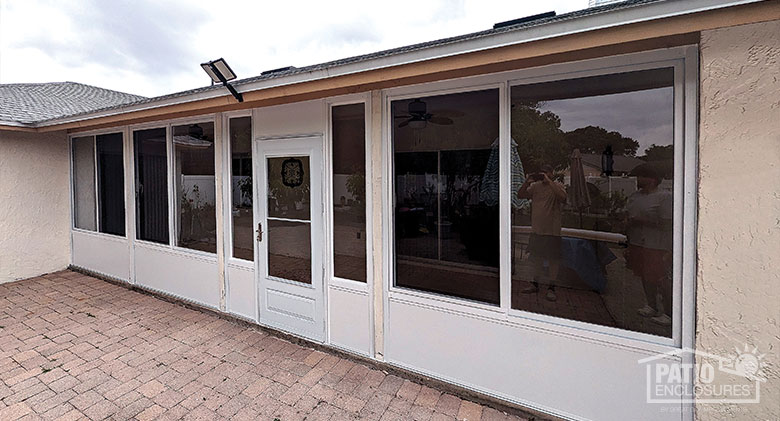 A white, glass porch or lanai enclosure with solid knee wall and a storm door in the middle.